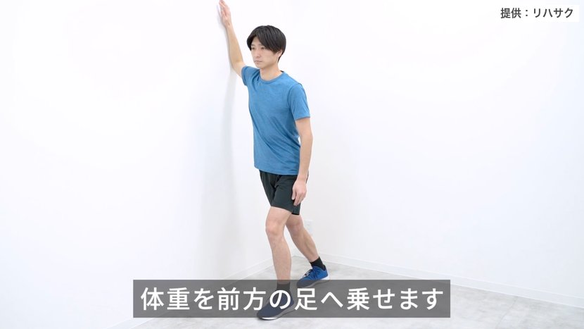 壁を使った大胸筋ストレッチ：腕を壁につけ、体重を前の足に乗せて胸の前を伸ばす